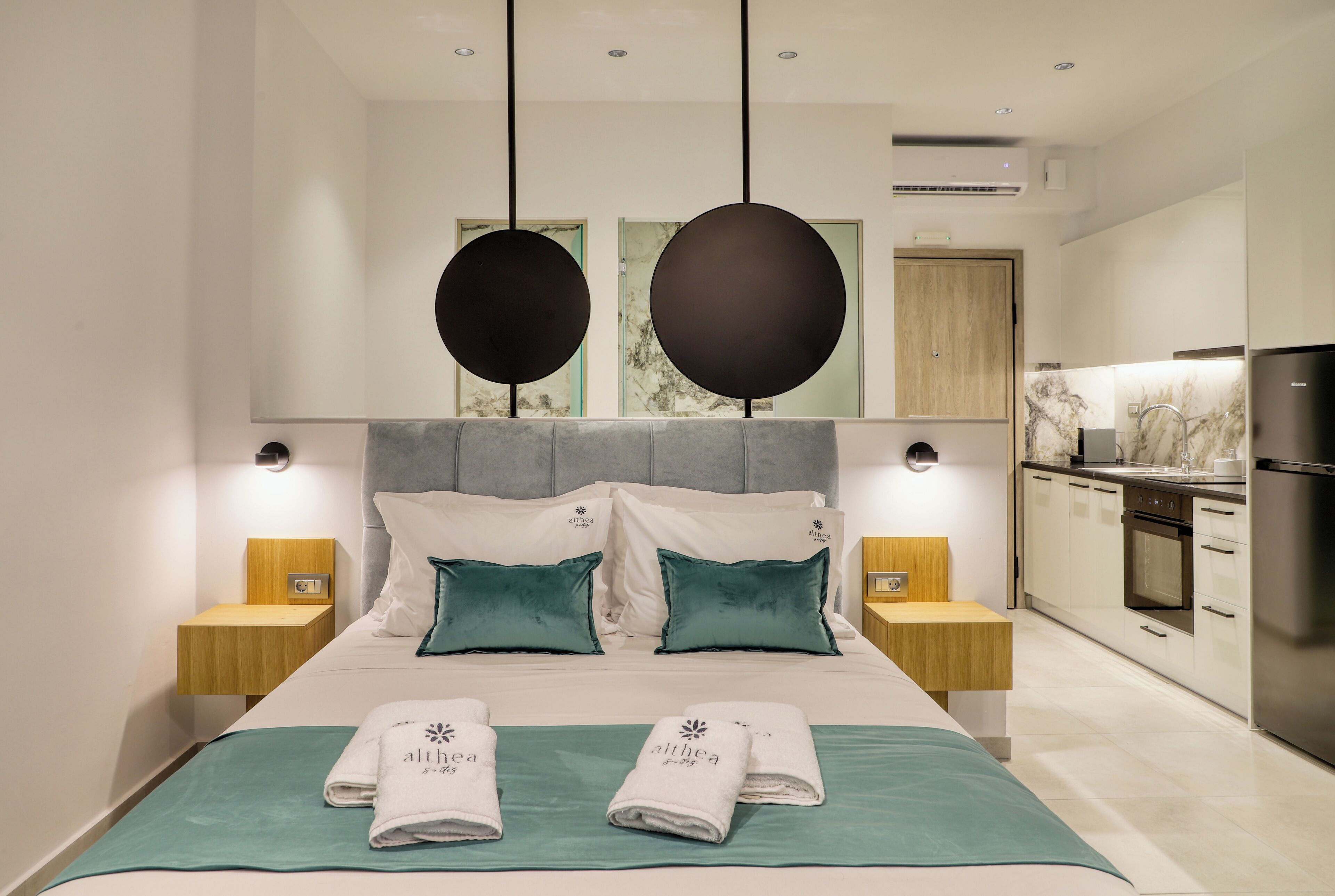 Une chambre d’hôtel moderne dotée d’un grand lit, de deux tables de chevet, d’une armoire intégrée, d’un coin cuisine et d’une salle de bain.