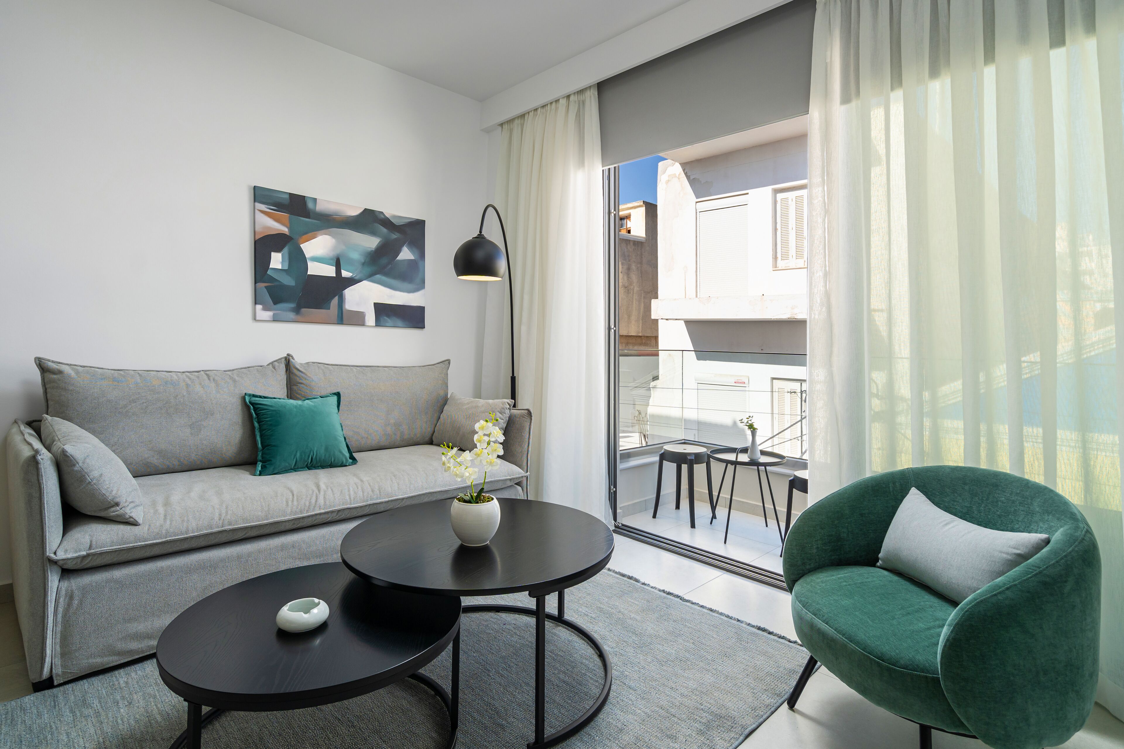 Una sala de estar moderna con un sofá gris, un sillón verde, una mesa de centro redonda negra y una lámpara de pie.