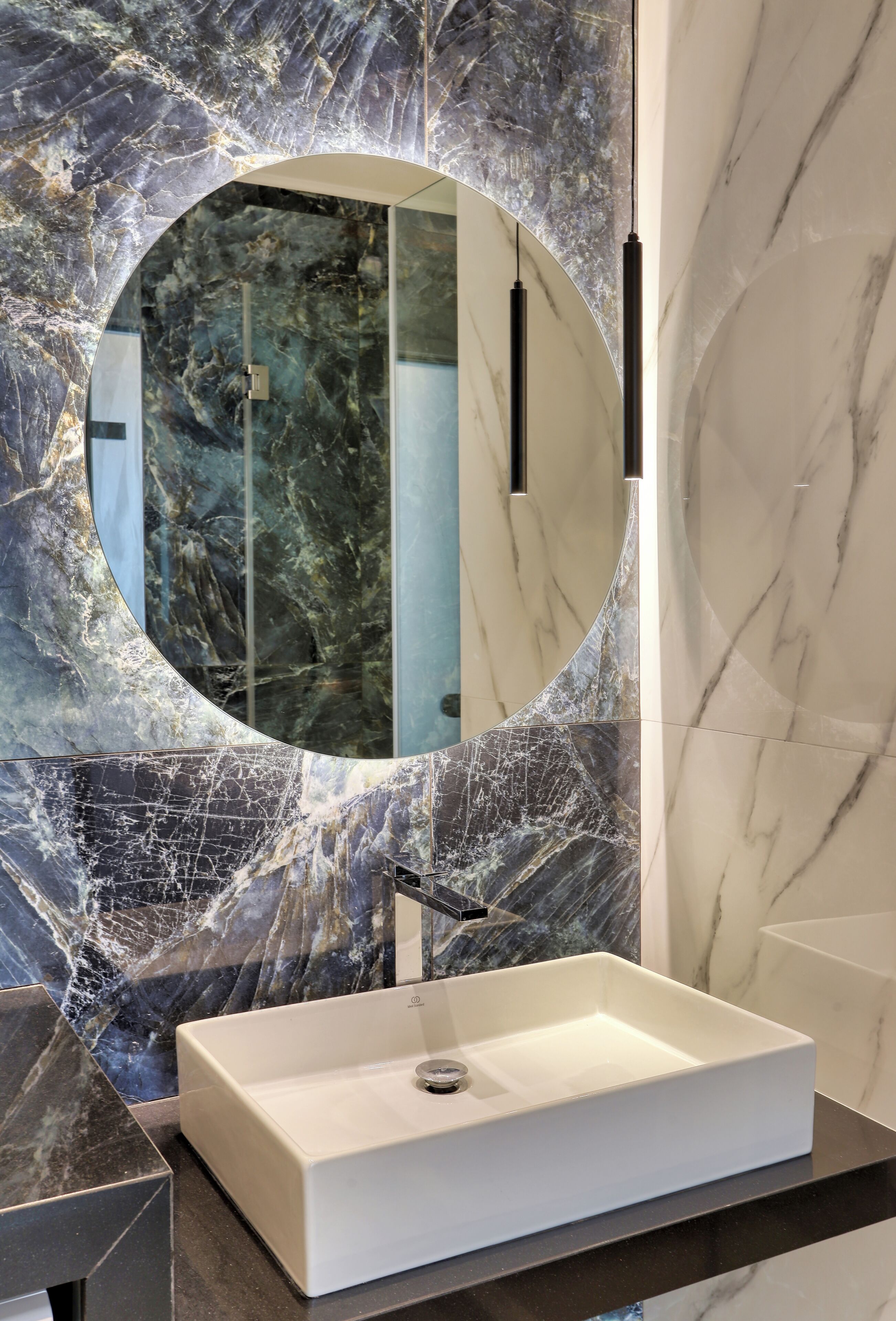 A bathroom with a white sink, a large mirror, and marble walls.
