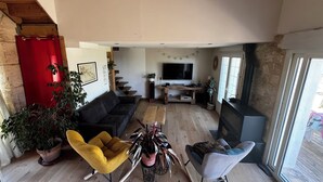 A cozy living room with a sofa, two rocking chairs, a coffee table, and a TV. There are plants and a fireplace.
