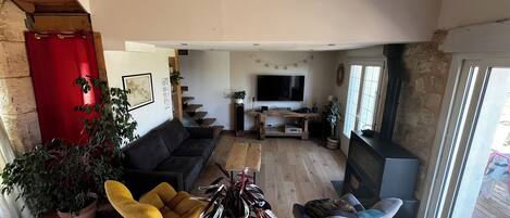 A cozy living room with a sofa, two rocking chairs, a coffee table, and a TV. There are plants and a fireplace.