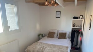 A bedroom with a bed, a bedside table, a window, a shelf with items, and a closet.