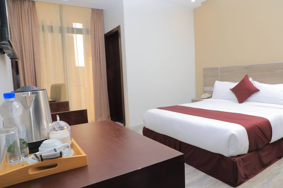 A hotel room with a bed, a wooden desk, a tray with toiletries, and a TV.