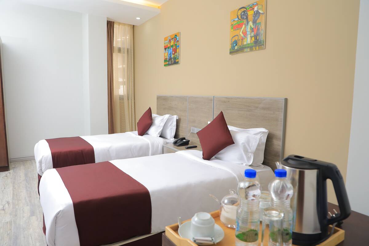 A hotel room with two beds, a nightstand, a coffee maker, and a tray with breakfast items.