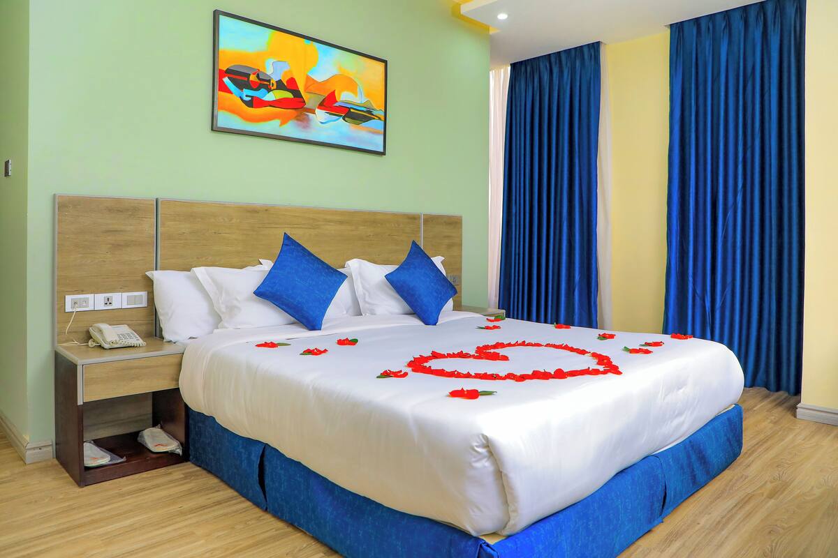 A hotel room with a bed, a nightstand, a painting on the wall, and blue curtains.