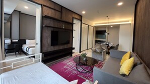 Ein modernes Hotelzimmer mit einem großen Bett, einem an der Wand montierten Fernseher, einem Essbereich und einer Sitzecke mit Sofa und Couchtisch.