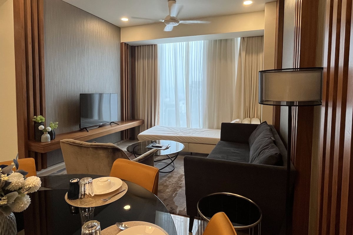 Ein Hotelzimmer mit Esstisch für zwei Personen, einer Couch, einem Fernseher und einem Deckenventilator.