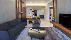 Ein modernes Wohnzimmer mit einer Couch, Hocker und einem Fernseher auf einem Holzständer.