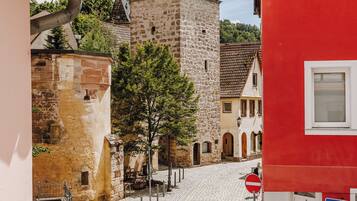 Una calle empedrada con edificios históricos de piedra, una torre del reloj y un edificio rojo con una puerta.