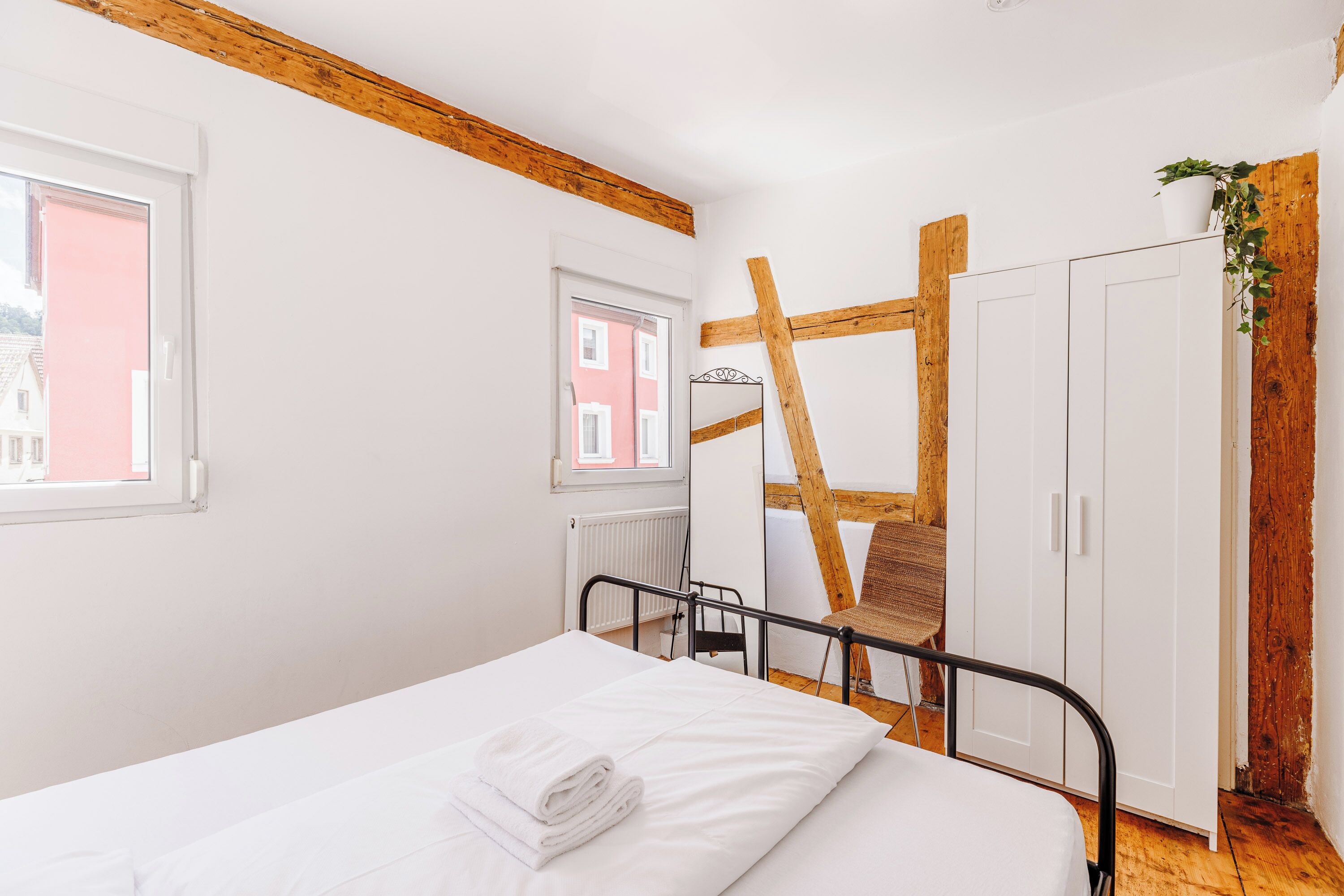 Une chambre à coucher avec un lit, un radiateur, une fenêtre, une chaise en bois et une armoire.