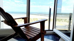 A wooden chair by a large window with a view of the beach and ocean. - Seaview Apartment in Nieuwpoort (Nieuwpoort)