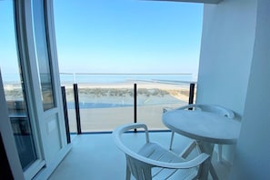 A balcony with a view of a beach and a pier, a white table, and a white chair.