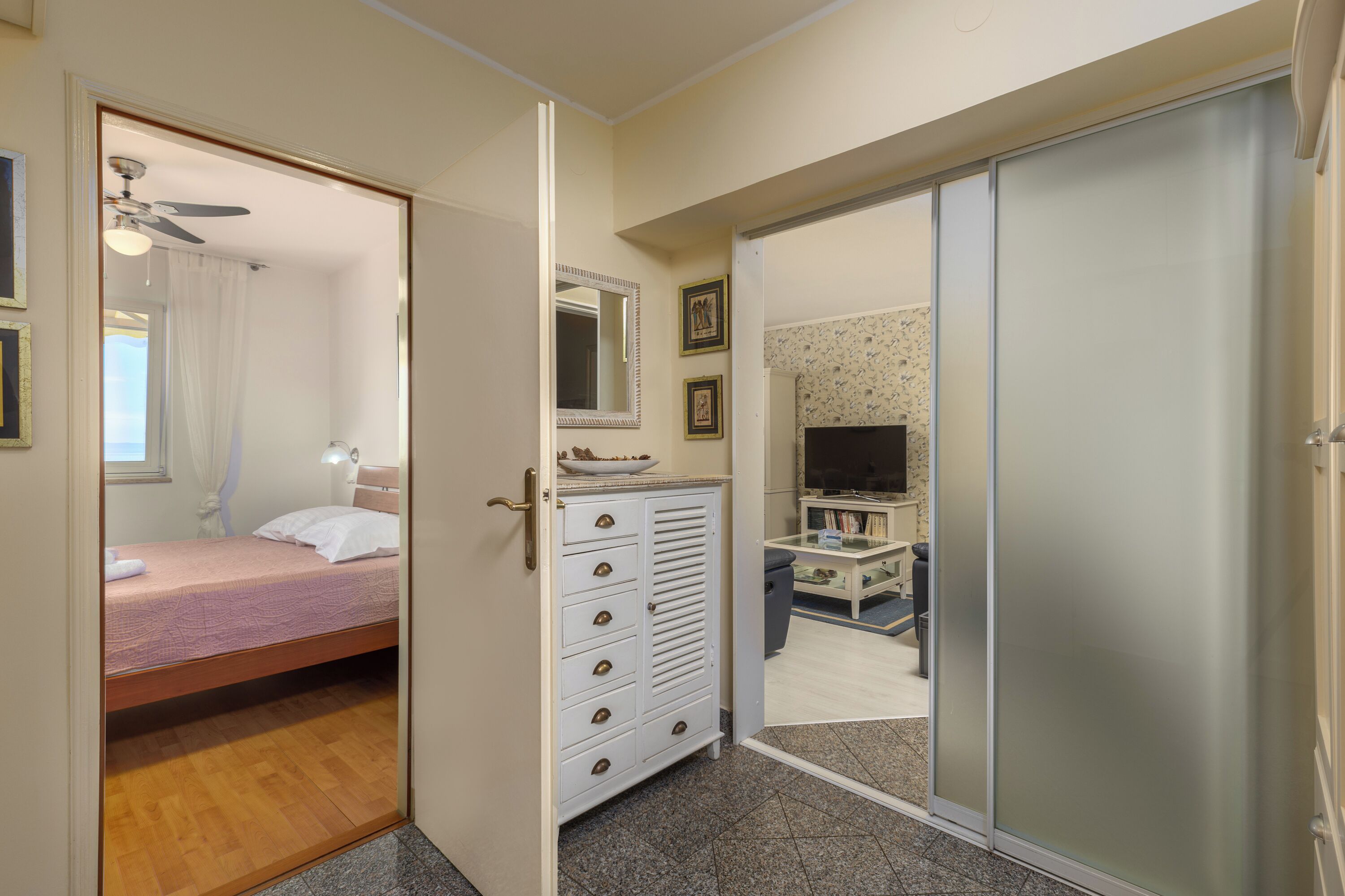 A bedroom with a bed, a dresser, a mirror, and a television in the adjacent room.
