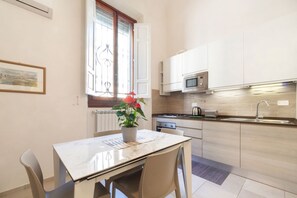 Une cuisine moderne avec des meubles blancs, un four à micro-ondes et une fenêtre équipée de stores.