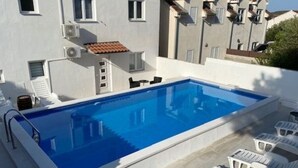 A rectangular swimming pool with a white border, surrounded by white lounge chairs and a small table. - Villa Brazza (Milna)