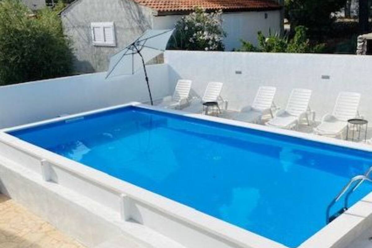 Ein Pool auf dem Dach mit klarem, blauem Wasser, umgeben von weißen Liegestühlen und einer weißen Mauer.