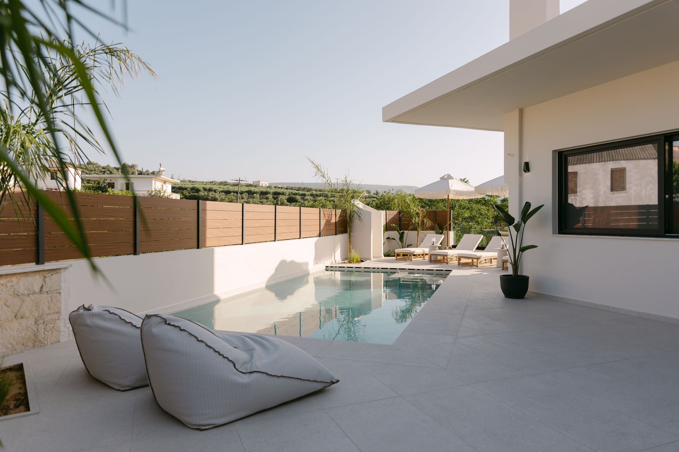 Un espace piscine extérieur moderne, doté de chaises longues et d’une plante en pot.