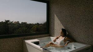 En kvinna som kopplar av i ett modernt badkar på ett spa, med utsikt över staden genom ett stort fönster.