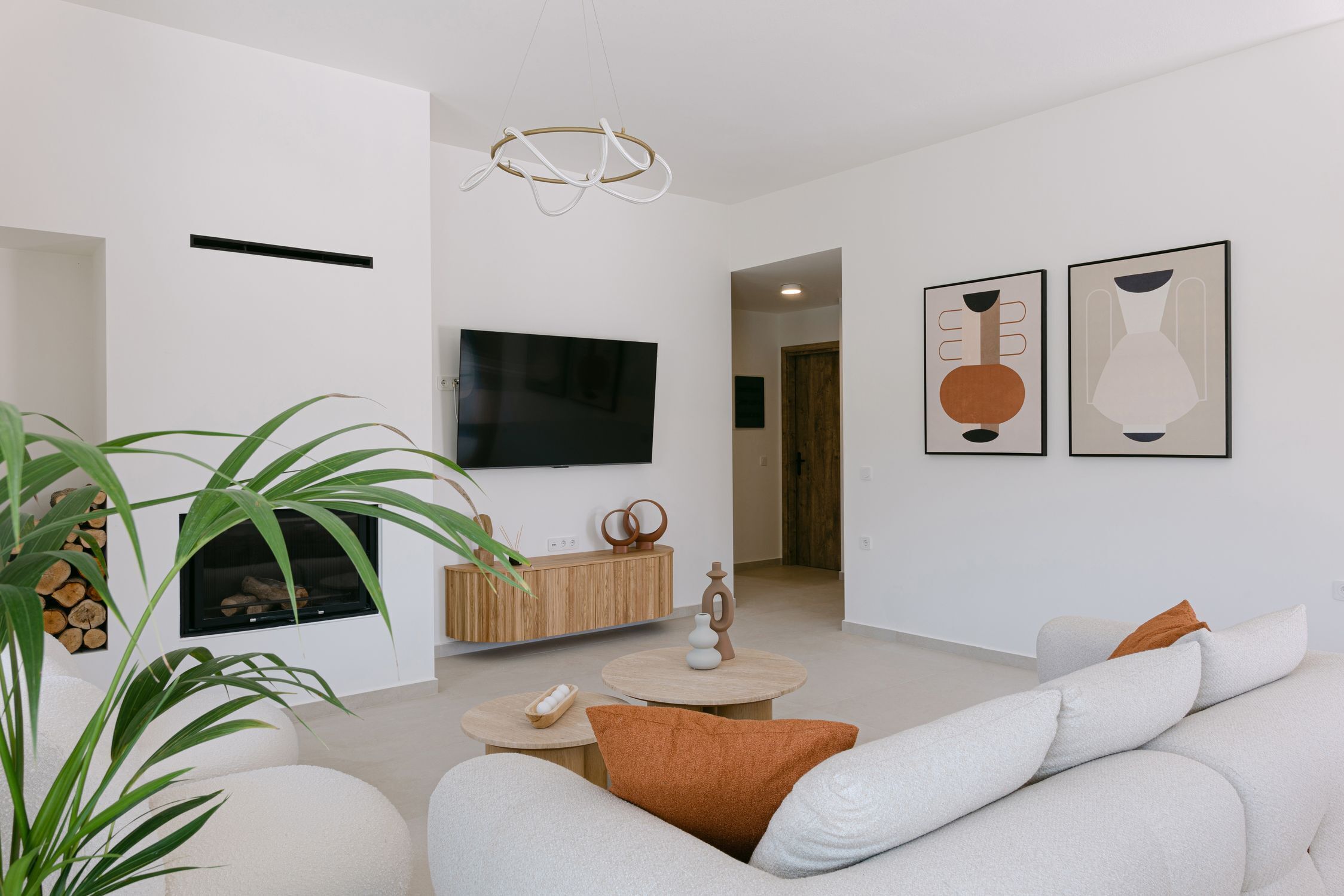 A modern living room with a flat-screen TV, a fireplace, a round coffee table, and a sofa with cushions.