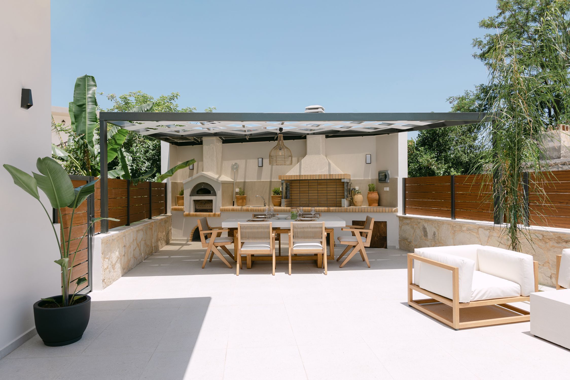 Een terras buiten met een eettafel, stoelen, een houten bank en een barbecuehoek.