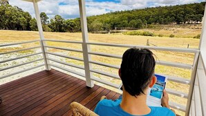 A person sitting on a wooden deck chair under a white pergola, reading a book.