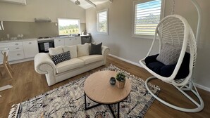 A modern living room with a sofa, a hanging chair, a round table, and a kitchen in the background.