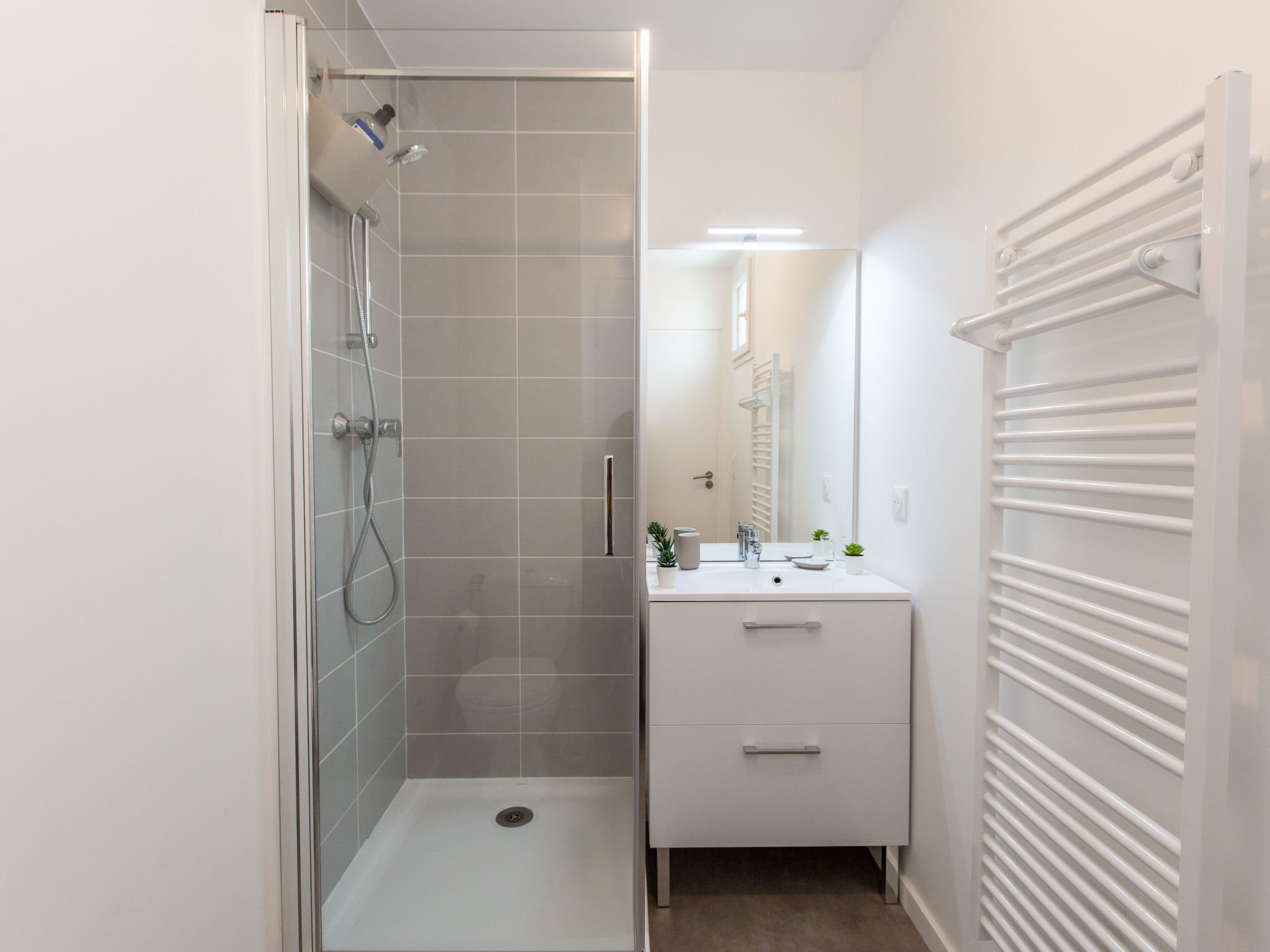 A modern bathroom with a glass shower enclosure, a white vanity with a mirror, and a towel rack.