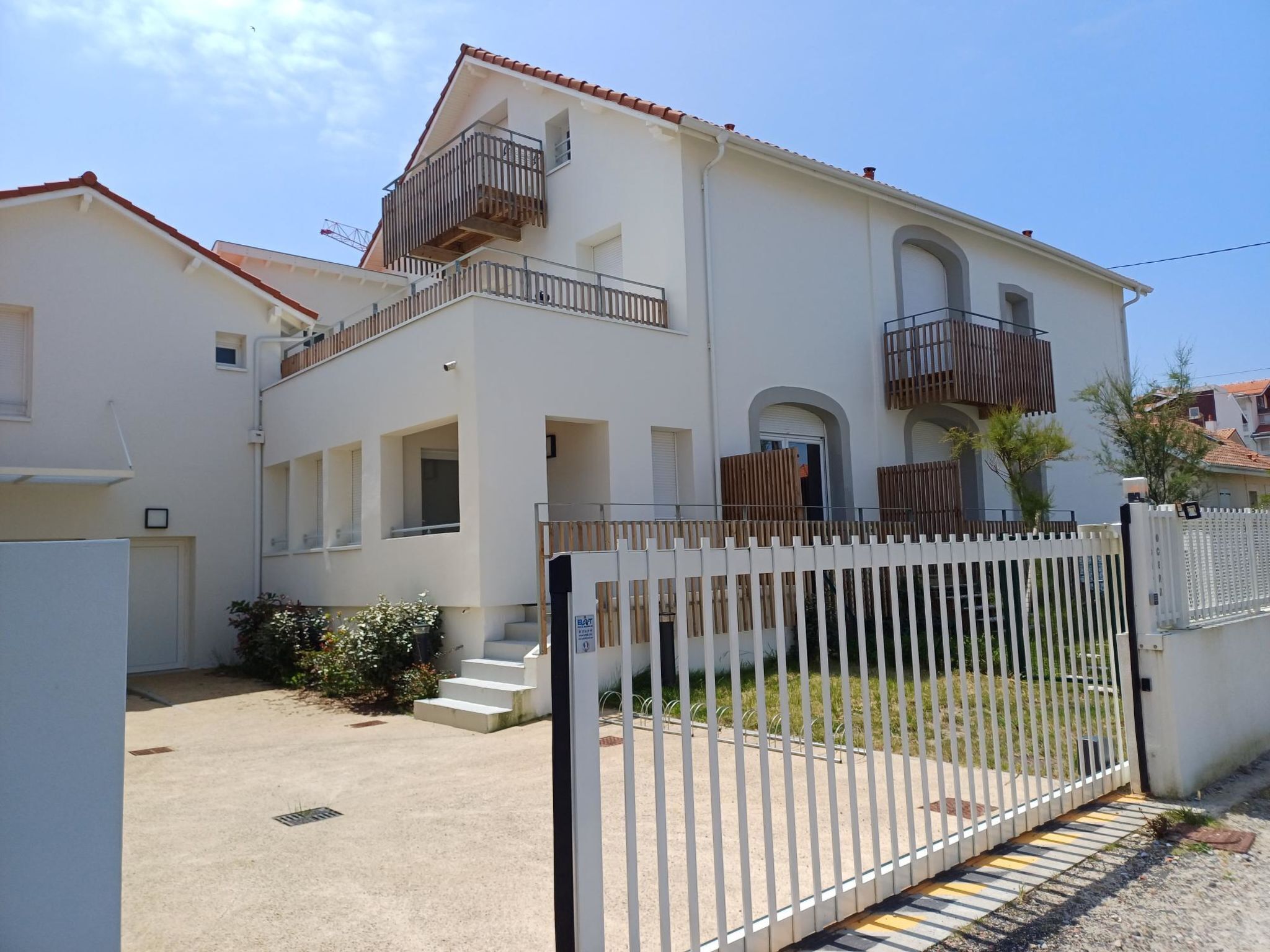 A two-story residential building with a white exterior, a balcony on the upper floor, and a gated entrance.