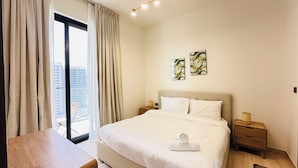 Habitación de hotel con una cama grande, una mesita de noche de madera y una vista de la ciudad a través de un ventanal amplio.