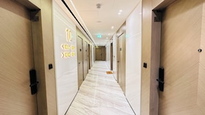 Un pasillo de hotel con piso de mármol, puertas numeradas y un letrero que indica la dirección de las habitaciones.