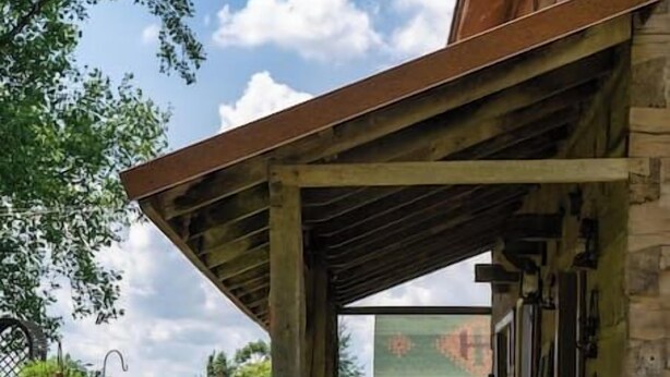 A covered outdoor area with a wooden deck, surrounded by a garden with various plants and flowers. - Vintage 1850's Log Cabin Glamping (Flora)