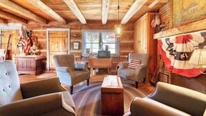 A rustic log cabin interior with a cozy seating area, wooden beams, and American flags. - Vintage 1850's Log Cabin Glamping (Flora)