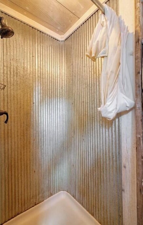 A bathroom with a corrugated wall, a shower area, and hanging clothes.