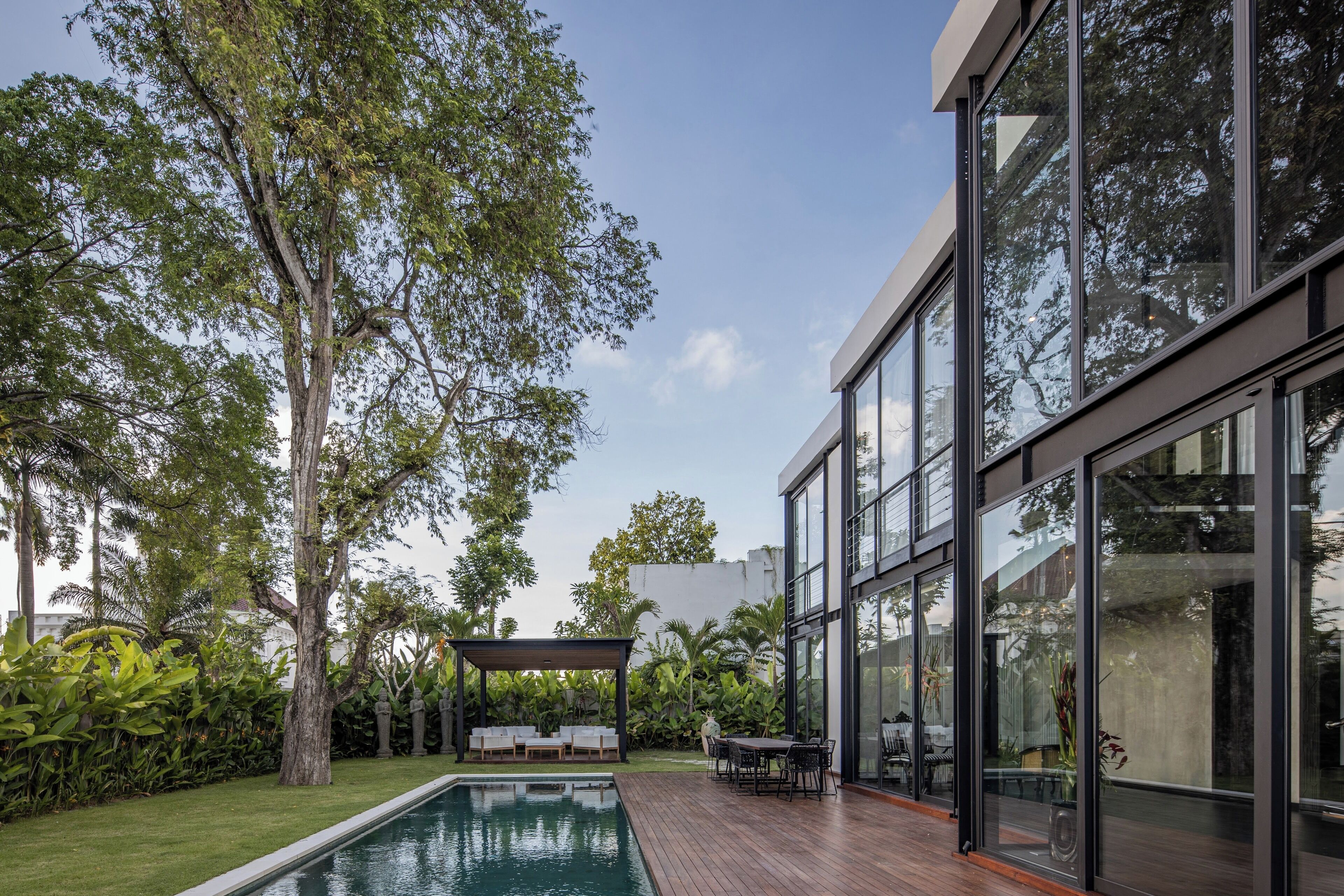 Uma área de piscina moderna ao ar livre, com um deck de madeira, espreguiçadeiras e um pergolado.