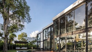 A modern building with large glass windows, a pool, and outdoor seating. - Villa Gima 1 (Kerobokan)