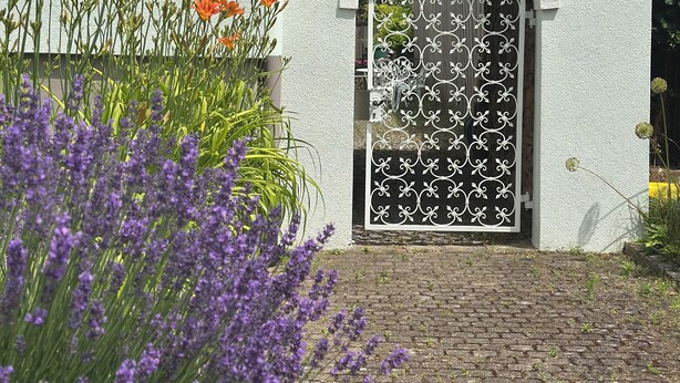 A building with a white exterior, a tiled roof, a brick pathway, and a decorative metal gate.