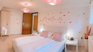 A bedroom with a large bed, a bedside table, a nightstand, a wardrobe, and a door.