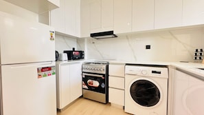 A compact kitchen with a built-in washing machine, a stove, and a refrigerator. - OYO 1290 Home Fully Furnished 1bed Apartment @JVC (Dubai)