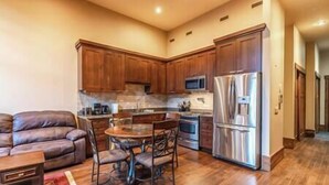 A modern kitchen with wooden cabinets, a stainless steel refrigerator, and a dining area with a glass table and chairs.