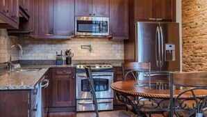 A kitchen with wooden cabinets, a stainless steel stove, a refrigerator, and a brick wall.