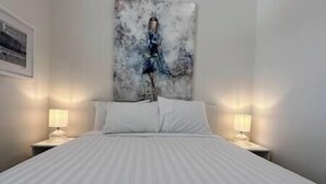 A hotel room with a large bed, two bedside tables with lamps, and a painting on the wall. - 6 min to Ski Hill / New & Modern / In Town (Fernie)