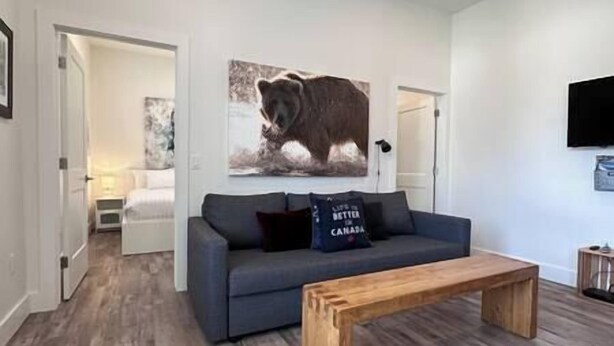 A modern living room with a grey sofa, a wooden coffee table, and a bear-themed artwork on the wall. - 6 min to Ski Hill / New & Modern / In Town (Fernie)
