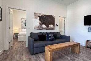 A modern living room with a grey sofa, a wooden coffee table, and a bear-themed artwork on the wall.