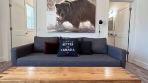 A living room with a grey sofa, a wooden coffee table, and a bear-themed pillow. - 6 min to Ski Hill / New & Modern / In Town (Fernie)
