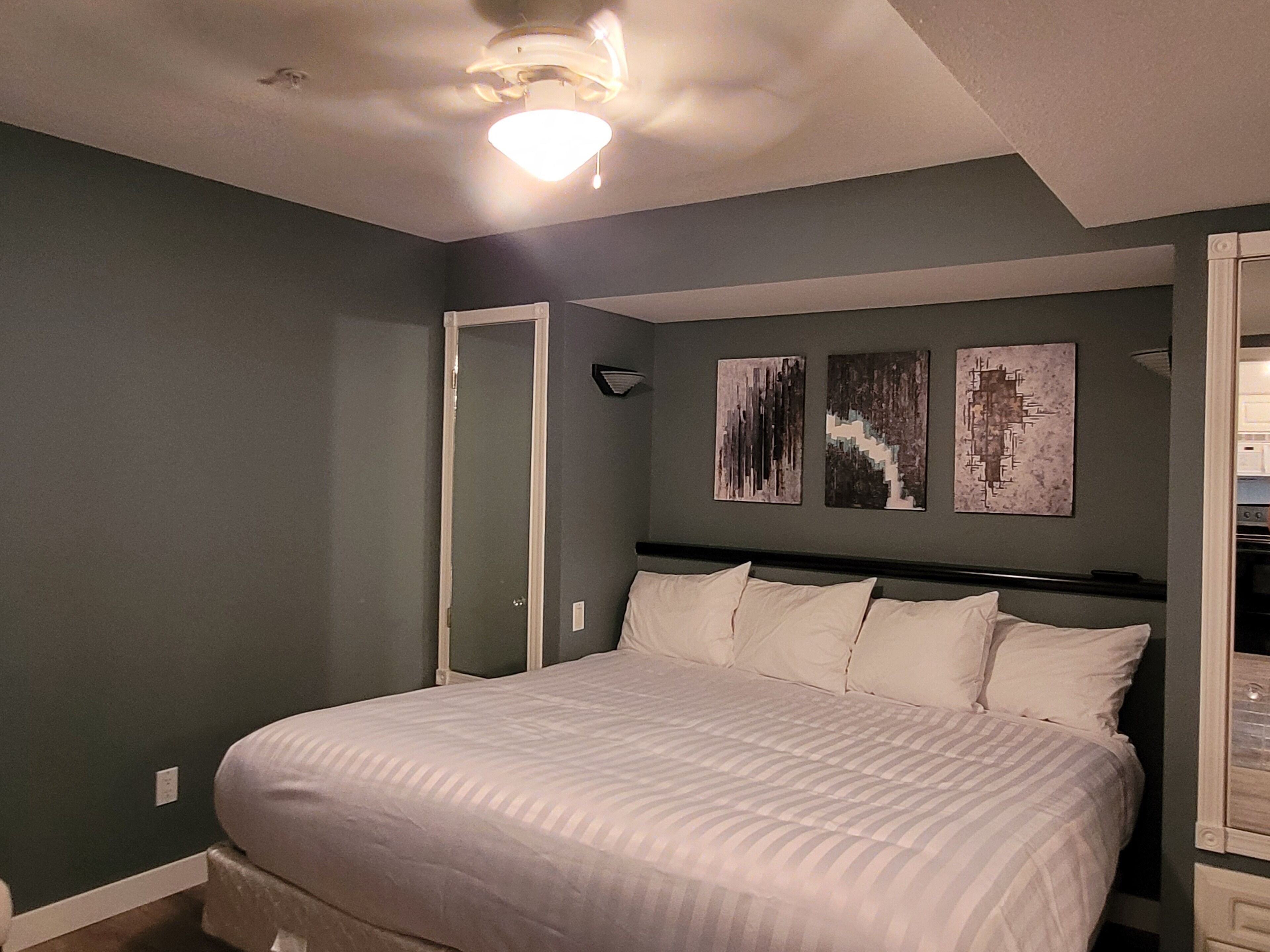 A bedroom with a bed, a ceiling fan, and two wall-mounted artworks.