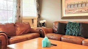 A living room with a brown leather sofa, a wooden coffee table, and a painting on the wall.