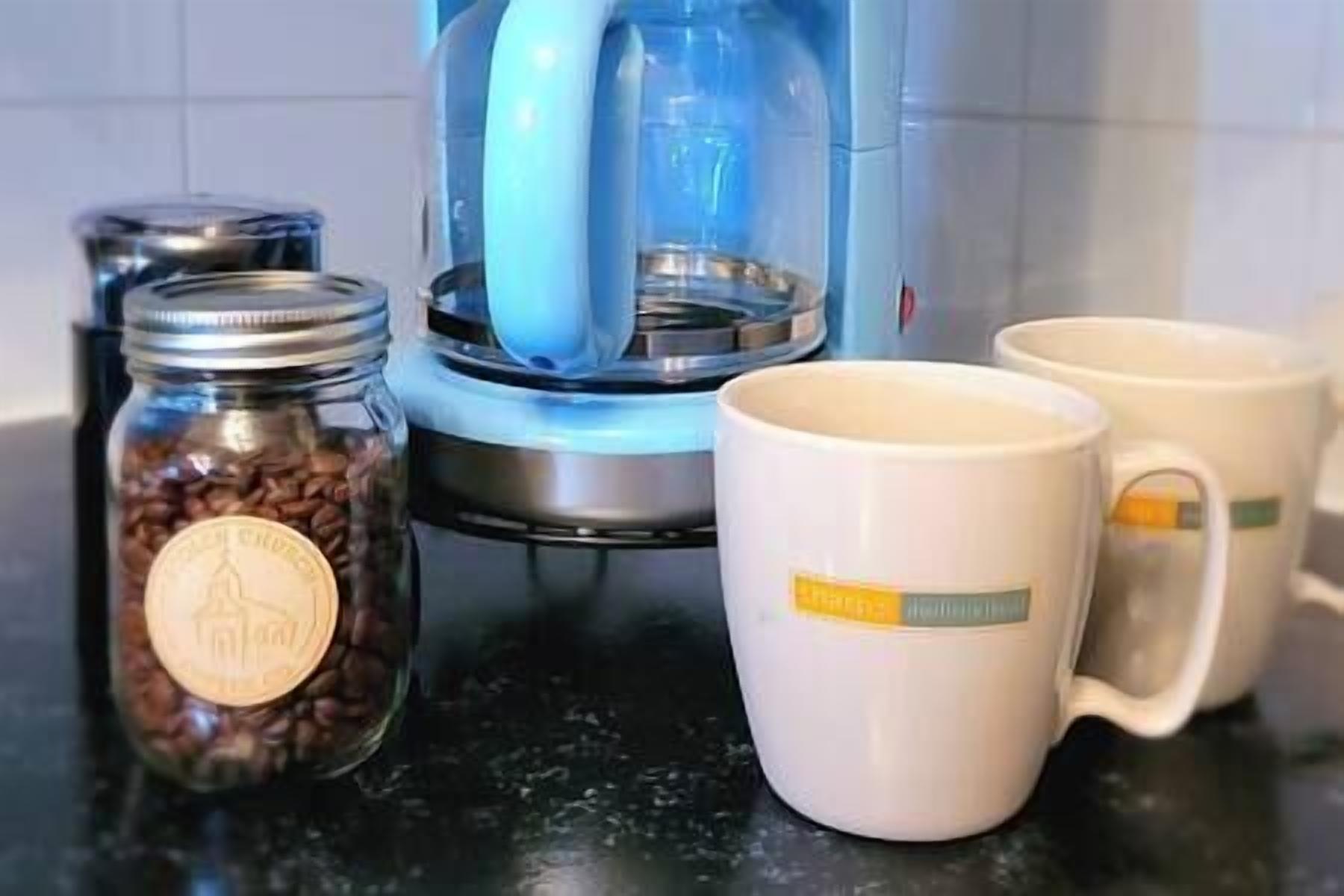 Un plan de travail de cuisine avec une machine à café, deux tasses à café et un bocal de grains de café.