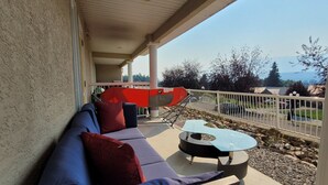 A covered outdoor seating area with a sofa and a table, overlooking a residential street and a body of water.