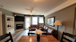 A living room with a wooden dining table, two sofas, a TV, a fireplace, and a ceiling fan.