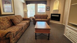 A living room with a sofa set, a coffee table, a fireplace, and a window with blinds. - Mountain View Condo with Sofabed and Aircon (Fairmont Hot Springs)